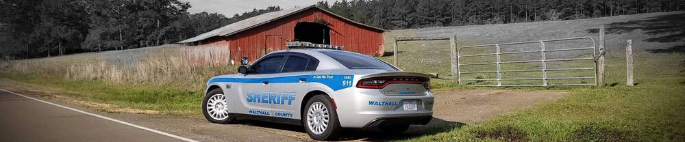 Walthall County Sheriff's vehicle parked on the side of the road and beside a red abandoned barn.